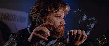 Movie still from “The Thing” (1982), directed by John Carpenter – A man with long hair and a long beard smoking a cigarette; Close Up shot, Low angle