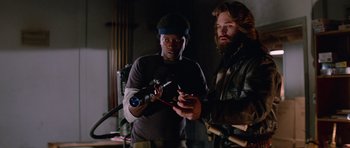 Movie still from “The Thing” (1982), directed by John Carpenter – Two men looking at their cell phones in the dark; Medium shot, Low angle