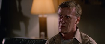 Movie still from “The Thing” (1982), directed by John Carpenter – A person sitting on a couch in a living room; Close Up shot, Over the shoulder angle