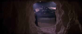 Movie still from “The Thing” (1982), directed by John Carpenter – An airplane is seen through a window in a cave; Extreme Wide shot, High angle
