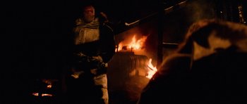 Movie still from “The Thing” (1982), directed by John Carpenter – A man standing in front of a burning building at night; Medium shot, Over the shoulder angle