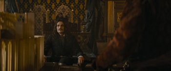 Movie still from “The Three Musketeers - Part I: D'Artagnan” (2023), directed by Martin Bourboulon – A man sitting on a chair in a room; Medium shot, Over the shoulder angle