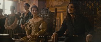 Movie still from “The Three Musketeers - Part I: D'Artagnan” (2023), directed by Martin Bourboulon – A man and a woman sitting on a wooden chair; Medium shot, Low angle