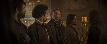 Movie still from “The Three Musketeers - Part I: D'Artagnan” (2023), directed by Martin Bourboulon – A group of men standing next to each other in a room; Medium shot, Over the shoulder angle