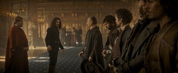 Movie still from “The Three Musketeers - Part I: D'Artagnan” (2023), directed by Martin Bourboulon – A group of men standing in a room; Wide shot, Over the shoulder angle