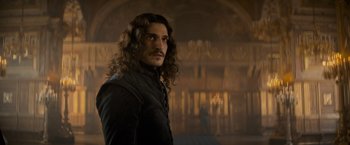 Movie still from “The Three Musketeers - Part I: D'Artagnan” (2023), directed by Martin Bourboulon – A man with long curly hair standing in front of a building; Close Up shot, Low angle