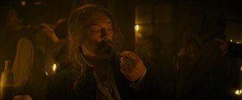 Movie still from “The Three Musketeers - Part I: D'Artagnan” (2023), directed by Martin Bourboulon – A man with long white hair is eating something; Close Up shot, Low angle