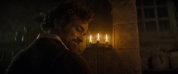 Movie still from “The Three Musketeers - Part I: D'Artagnan” (2023), directed by Martin Bourboulon – A man sitting in front of a lit candle in a room; Close Up shot, Over the shoulder angle