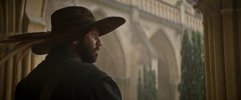 Movie still from “The Three Musketeers - Part I: D'Artagnan” (2023), directed by Martin Bourboulon – A man with a beard wearing a brown hat; Medium shot, Low angle