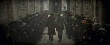 Movie still from “The Three Musketeers - Part I: D'Artagnan” (2023), directed by Martin Bourboulon – A group of men in hats are walking down the street; Wide shot, Over the shoulder angle