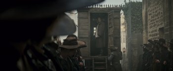 Movie still from “The Three Musketeers - Part I: D'Artagnan” (2023), directed by Martin Bourboulon – A group of people standing around a wooden house; Wide shot, Low angle
