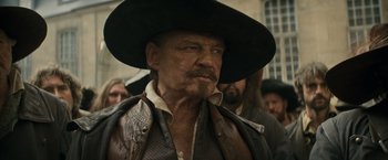 Movie still from “The Three Musketeers - Part I: D'Artagnan” (2023), directed by Martin Bourboulon – A man in a hat and a leather vest; Close Up shot, Over the shoulder angle