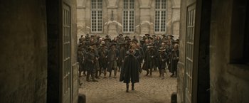 Movie still from “The Three Musketeers - Part I: D'Artagnan” (2023), directed by Martin Bourboulon – A group of men in hats and coats standing in front of a building; Wide shot, High angle