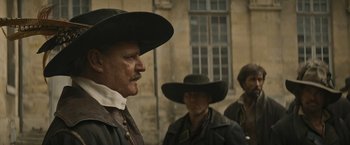 Movie still from “The Three Musketeers - Part I: D'Artagnan” (2023), directed by Martin Bourboulon – A man in a cowboy hat standing next to another man; Medium shot, Over the shoulder angle