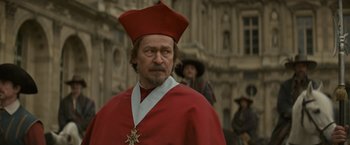 Movie still from “The Three Musketeers - Part I: D'Artagnan” (2023), directed by Martin Bourboulon – A man in a red robe and a red hat; Close Up shot, Over the shoulder angle