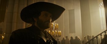 Movie still from “The Three Musketeers - Part I: D'Artagnan” (2023), directed by Martin Bourboulon – A man with a long beard wearing a large hat; Close Up shot, Low angle
