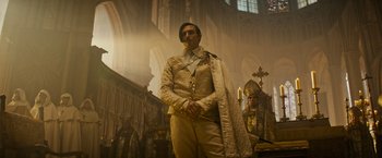 Movie still from “The Three Musketeers - Part I: D'Artagnan” (2023), directed by Martin Bourboulon – A man standing in front of a large cathedral; Medium shot, Low angle