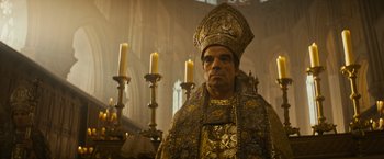 Movie still from “The Three Musketeers - Part I: D'Artagnan” (2023), directed by Martin Bourboulon – A man in a gold and black outfit standing in front of candles; Medium shot, Low angle