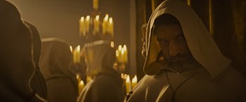 Movie still from “The Three Musketeers - Part I: D'Artagnan” (2023), directed by Martin Bourboulon – A man with a beard is sitting in front of candles; Medium shot, Over the shoulder angle