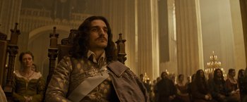 Movie still from “The Three Musketeers - Part I: D'Artagnan” (2023), directed by Martin Bourboulon – A man with long brown hair sitting in a chair; Medium shot, Low angle