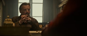 Movie still from “The Three Musketeers - Part I: D'Artagnan” (2023), directed by Martin Bourboulon – A man sitting at a table with a cigarette in his mouth; Medium shot, Over the shoulder angle