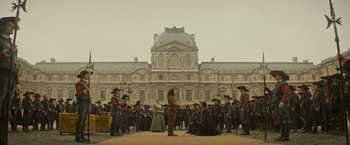 Movie still from “The Three Musketeers - Part I: D'Artagnan” (2023), directed by Martin Bourboulon – A group of people standing in front of a building; Extreme Wide shot, Low angle