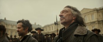 Movie still from “The Three Musketeers - Part I: D'Artagnan” (2023), directed by Martin Bourboulon – An old man looking up at a crowd of people; Close Up shot, Low angle