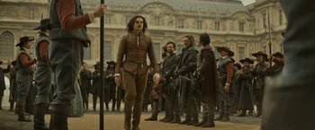 Movie still from “The Three Musketeers - Part I: D'Artagnan” (2023), directed by Martin Bourboulon – A group of people standing in front of a building; Wide shot, Over the shoulder angle