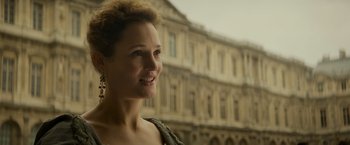 Movie still from “The Three Musketeers - Part I: D'Artagnan” (2023), directed by Martin Bourboulon – A woman standing in front of an old building; Close Up shot, Over the shoulder angle