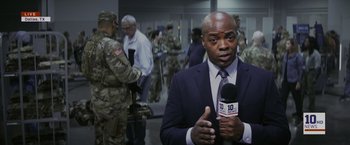 Movie still from “The Tomorrow War” (2021), directed by Chris McKay – A man in a suit and tie holding a microphone; Medium shot, Over the shoulder angle