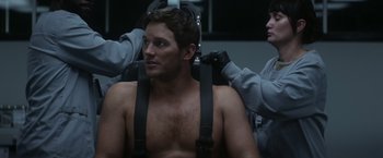 Movie still from “The Tomorrow War” (2021), directed by Chris McKay – A man sitting in a chair while another man adjusts the straps on him; Medium shot, Over the shoulder angle
