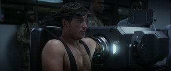 Movie still from “The Tomorrow War” (2021), directed by Chris McKay – A man with a head band is sitting in front of a projector; Medium shot, Over the shoulder angle