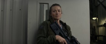 Movie still from “The Tomorrow War” (2021), directed by Chris McKay – A woman holding a gun while standing next to a wall; Medium shot, Over the shoulder angle