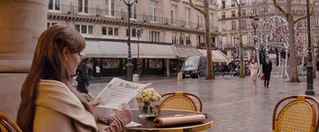 Movie still from “The Tourist” (2010), directed by Florian Henckel von Donnersmarck – A person sitting at a table with a newspaper and a vase of flowers; Medium shot, Over the shoulder angle