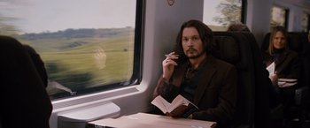 Movie still from “The Tourist” (2010), directed by Florian Henckel von Donnersmarck – A man sitting on a train holding a cigarette and reading a book; Medium shot, High angle
