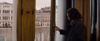 Movie still from “The Tourist” (2010), directed by Florian Henckel von Donnersmarck – A woman standing in front of a window looking out at a city; Medium shot, Over the shoulder angle