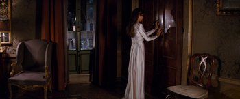 Movie still from “The Tourist” (2010), directed by Florian Henckel von Donnersmarck – A woman in a long white dress standing in front of a door; Wide shot, Over the shoulder angle