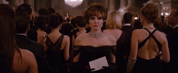 Movie still from “The Tourist” (2010), directed by Florian Henckel von Donnersmarck – A woman in a black dress holding an envelope in front of a group of people; Medium shot, Over the shoulder angle