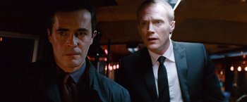 Movie still from “The Tourist” (2010), directed by Florian Henckel von Donnersmarck – A man in a suit and tie standing next to another man in a suit and tie; Close Up shot, Low angle