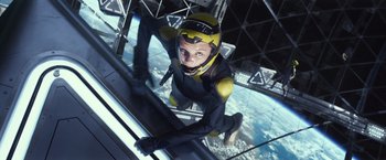 Movie still from “Ender's Game” (2013), directed by Gavin Hood – A man in a yellow and black suit hanging from a metal structure; Medium shot, Overhead angle