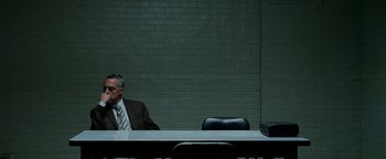 Movie still from “The Town” (2010), directed by Ben Affleck – A man sitting at a table in front of a brick wall; Wide shot, Over the shoulder angle