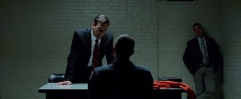 Movie still from “The Town” (2010), directed by Ben Affleck – A man in a suit and tie talking to another man in a suit and tie in front of a brick wall; Medium shot, Over the shoulder angle