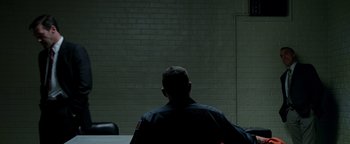 Movie still from “The Town” (2010), directed by Ben Affleck – A man sitting in front of a brick wall in a room; Wide shot, Over the shoulder angle