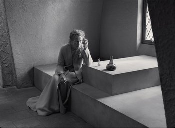Movie still from “The Tragedy of Macbeth” (2021), directed by Joel Coen – A woman sitting on steps in front of a window taking a picture; Wide shot, High angle