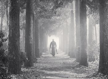 Movie still from “The Tragedy of Macbeth” (2021), directed by Joel Coen – A man walking down a path in the middle of a forest; Wide shot, Low angle