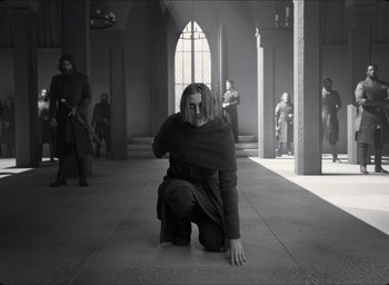 Movie still from “The Tragedy of Macbeth” (2021), directed by Joel Coen – A woman kneeling down in a church with people standing around; Wide shot, Low angle