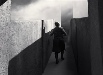 Movie still from “The Tragedy of Macbeth” (2021), directed by Joel Coen – A woman walking down a path between two concrete walls; Wide shot, Low angle