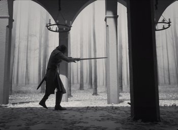 Movie still from “The Tragedy of Macbeth” (2021), directed by Joel Coen – A man dressed as a medieval knight with a sword in a forest; Wide shot, Low angle