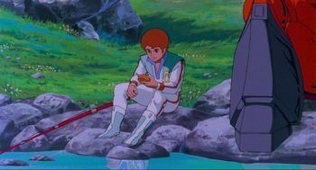 Movie still from “The Transformers: The Movie” (1986), directed by Nelson Shin – A man sitting on a rock in front of some water; Medium shot, High angle