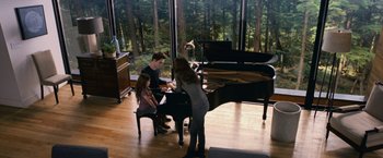 Movie still from “The Twilight Saga: Breaking Dawn - Part 2” (2012), directed by Bill Condon – A woman and two children are playing a piano in front of a large window; Wide shot, High angle